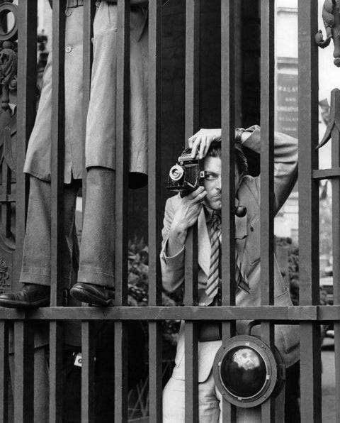 A photographer framed by iron bars focuses his camera, capturing a scene outside the confines of the barrier, takes a photograph through the railings at Admiralty Arch the day before Queen Elizabeth II's Coronation