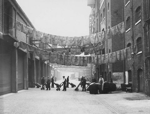 This photograph was taken at the North Quay, West India Docks and shows a gang of dockers trucking bags of sugar beneath an awning of washed sacks that are hung out for drying at.