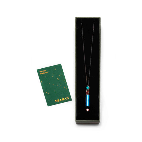 Necklace with a colourful pendant in a black box, accompanied by a green card on a white background