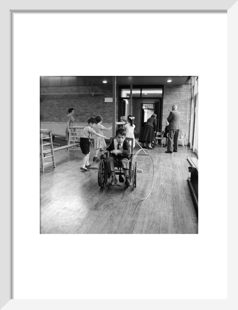 A disabled young boy using a wheelchair rolls a hoop along the floor during a physical education lesson at the 'FDR School for Handicapped Children', NW3