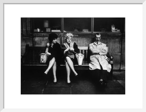 Two women and a man sit on a bench 1961