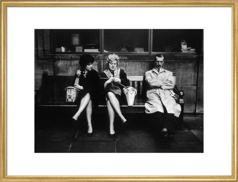 Two women and a man sit on a bench 1961