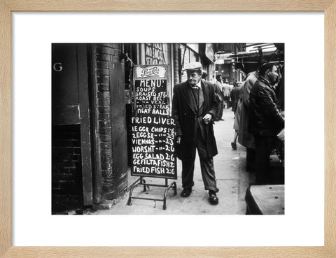 A man reads a chalk board on the street outside a cafe1961