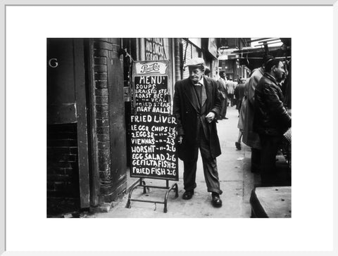 A man reads a chalk board on the street outside a cafe1961