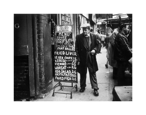 A man reads a chalk board on the street outside a cafe1961