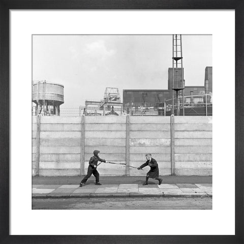 Two boys fighting with sticks in front of a concrete wall. c.1955