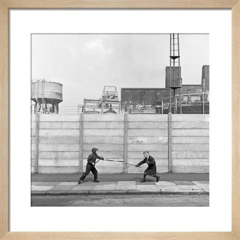 Two boys fighting with sticks in front of a concrete wall. c.1955