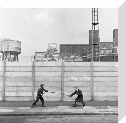Two boys fighting with sticks in front of a concrete wall. c.1955