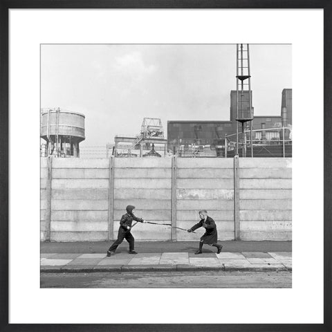 Two boys fighting with sticks in front of a concrete wall. c.1955
