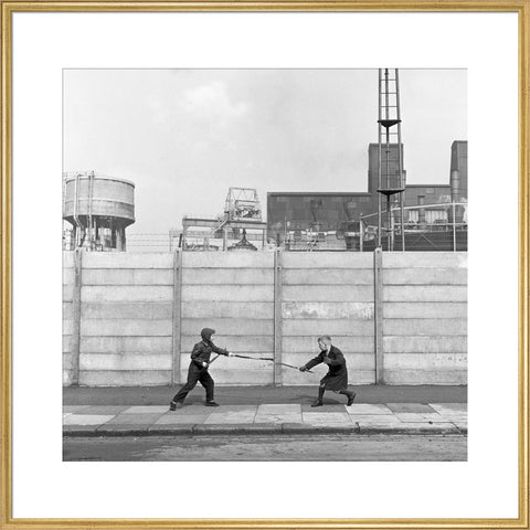 Two boys fighting with sticks in front of a concrete wall. c.1955
