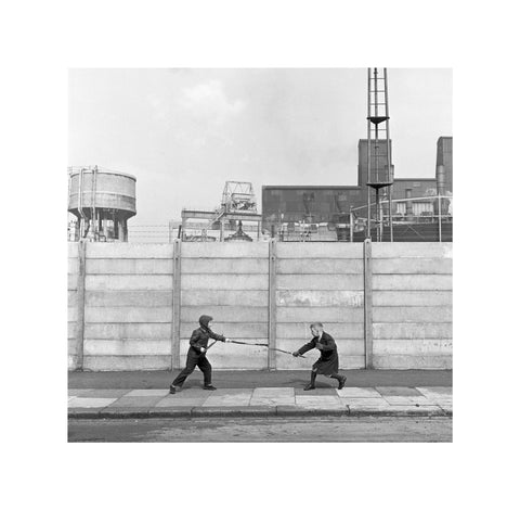 Two boys fighting with sticks in front of a concrete wall. c.1955