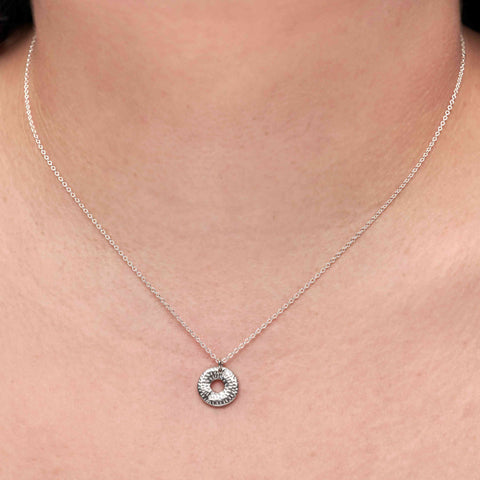 Silver necklace with a small round textured pendant on a person's neck