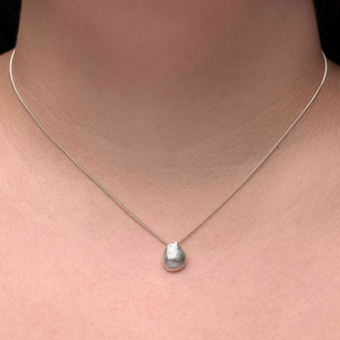 Close-up of a person wearing a silver irregular round pendant necklace. 