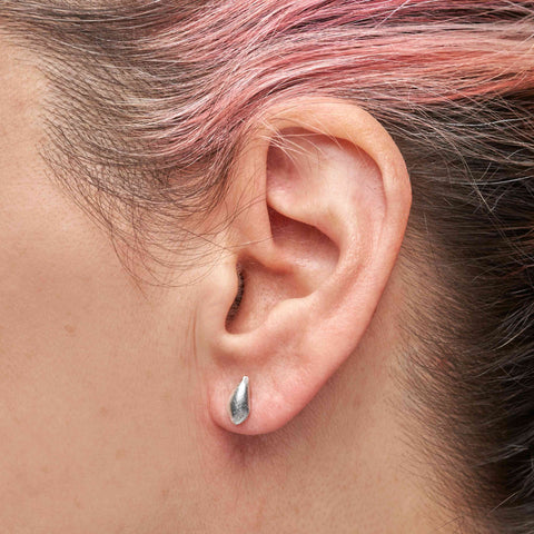 Close-up of a person with pink and brown hair wearing a silver teardrop-shaped stud earring.