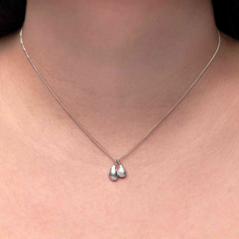 Close-up of a person wearing a silver necklace with two irregular teardrop-shaped pendants