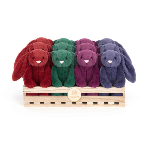 Four colorful plush bunnies in a wooden crate with a Jelly Cat brand label on a white background.