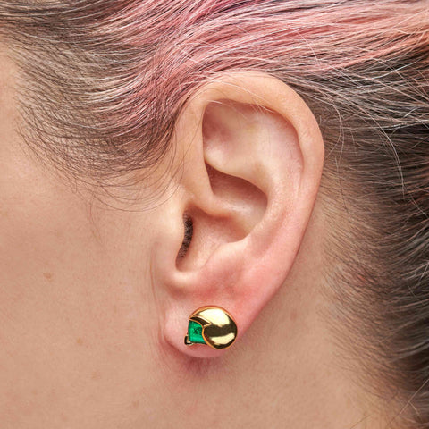 Gold earring with green e-waste insert worn by a person with pink hair.