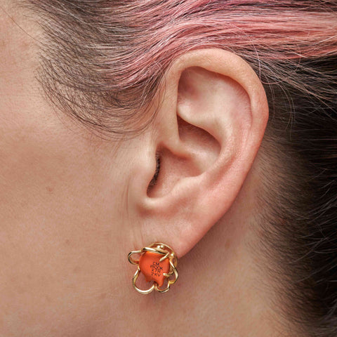 Close-up of a person with pink and brown hair wearing a gold earring with an orange centre. 