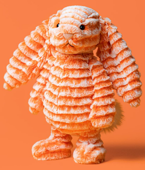 An orange and white striped plush bunny toy with long floppy ears, standing against a solid orange background.