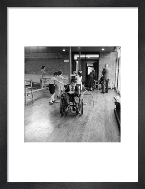 A disabled young boy using a wheelchair rolls a hoop along the floor during a physical education lesson at the 'FDR School for Handicapped Children', NW3