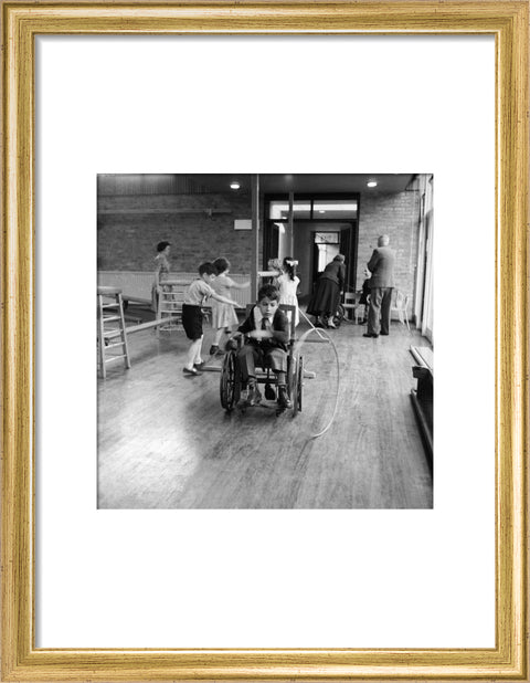 A disabled young boy using a wheelchair rolls a hoop along the floor during a physical education lesson at the 'FDR School for Handicapped Children', NW3