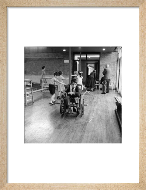 A disabled young boy using a wheelchair rolls a hoop along the floor during a physical education lesson at the 'FDR School for Handicapped Children', NW3
