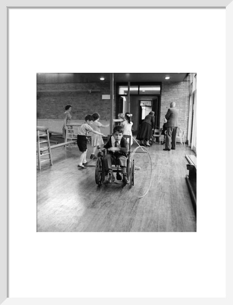 A disabled young boy using a wheelchair rolls a hoop along the floor during a physical education lesson at the 'FDR School for Handicapped Children', NW3