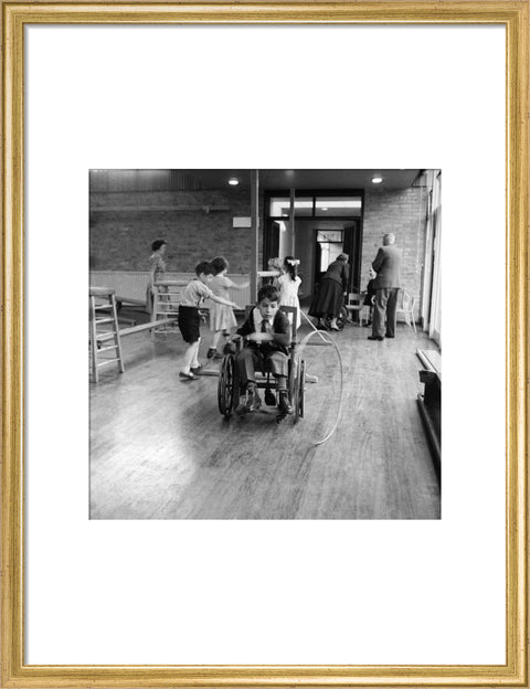 A disabled young boy using a wheelchair rolls a hoop along the floor during a physical education lesson at the 'FDR School for Handicapped Children', NW3
