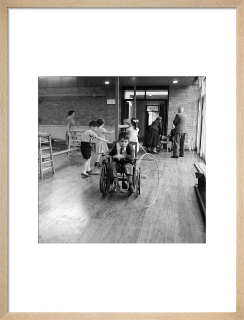A disabled young boy using a wheelchair rolls a hoop along the floor during a physical education lesson at the 'FDR School for Handicapped Children', NW3