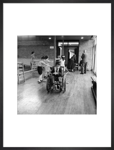 A disabled young boy using a wheelchair rolls a hoop along the floor during a physical education lesson at the 'FDR School for Handicapped Children', NW3