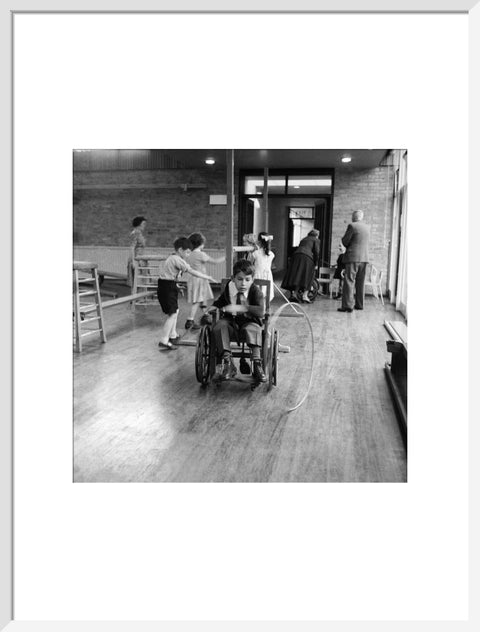 A disabled young boy using a wheelchair rolls a hoop along the floor during a physical education lesson at the 'FDR School for Handicapped Children', NW3