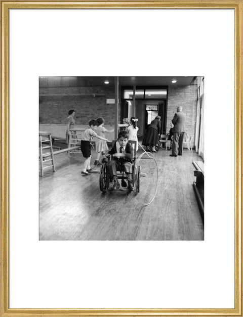 A disabled young boy using a wheelchair rolls a hoop along the floor during a physical education lesson at the 'FDR School for Handicapped Children', NW3