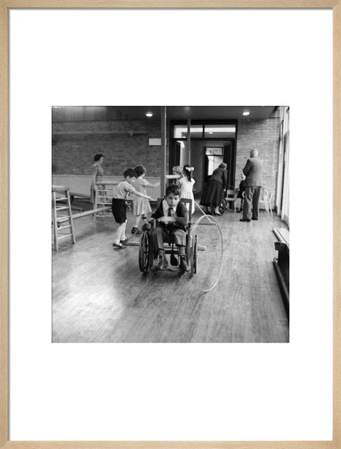 A disabled young boy using a wheelchair rolls a hoop along the floor during a physical education lesson at the 'FDR School for Handicapped Children', NW3