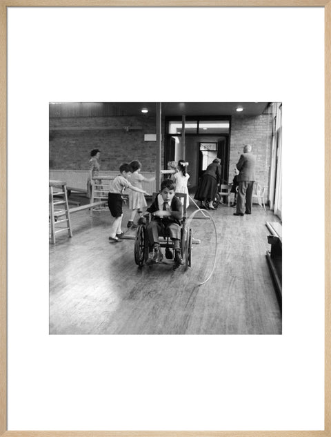 A disabled young boy using a wheelchair rolls a hoop along the floor during a physical education lesson at the 'FDR School for Handicapped Children', NW3