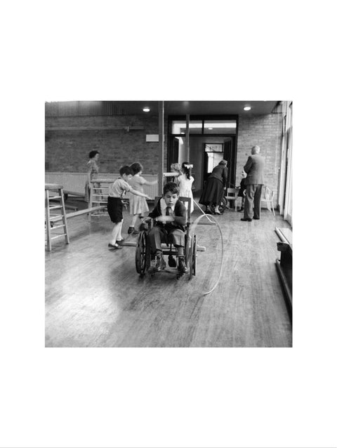 A disabled young boy using a wheelchair rolls a hoop along the floor during a physical education lesson at the 'FDR School for Handicapped Children', NW3