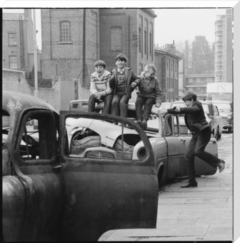 Four boys play on wrecked cars parked in the street 1967