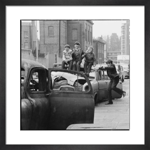 Four boys play on wrecked cars parked in the street 1967