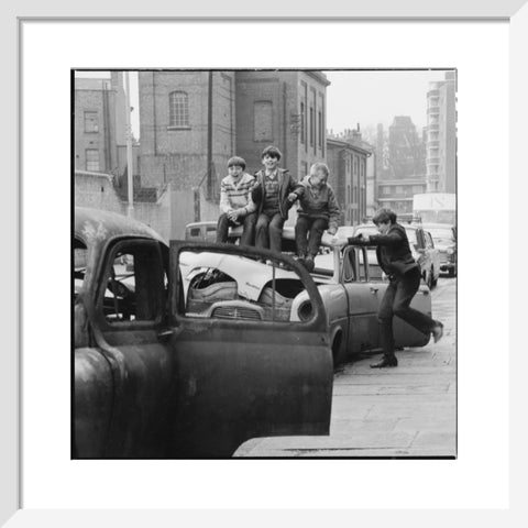 Four boys play on wrecked cars parked in the street 1967