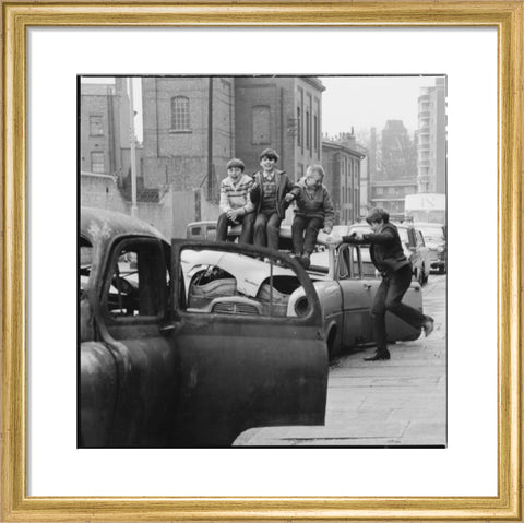 Four boys play on wrecked cars parked in the street 1967