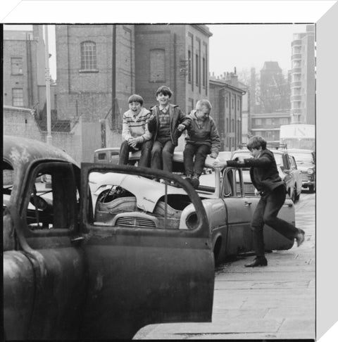 Four boys play on wrecked cars parked in the street 1967