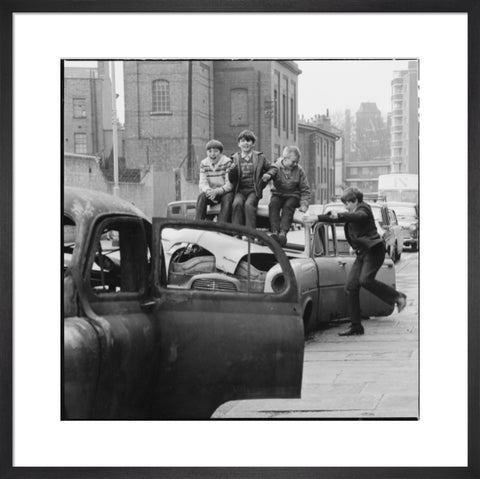 Four boys play on wrecked cars parked in the street 1967