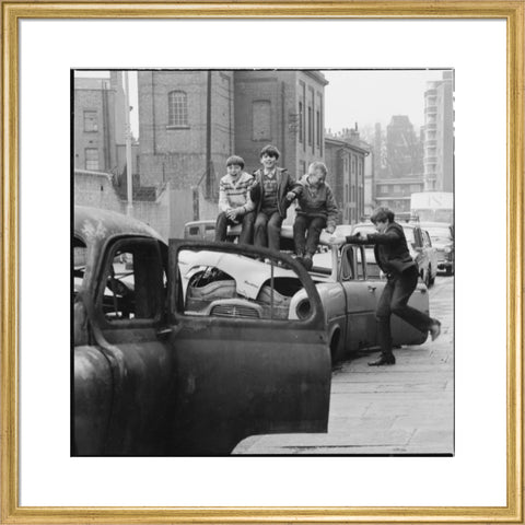 Four boys play on wrecked cars parked in the street 1967