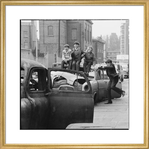 Four boys play on wrecked cars parked in the street 1967