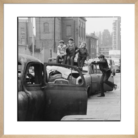 Four boys play on wrecked cars parked in the street 1967