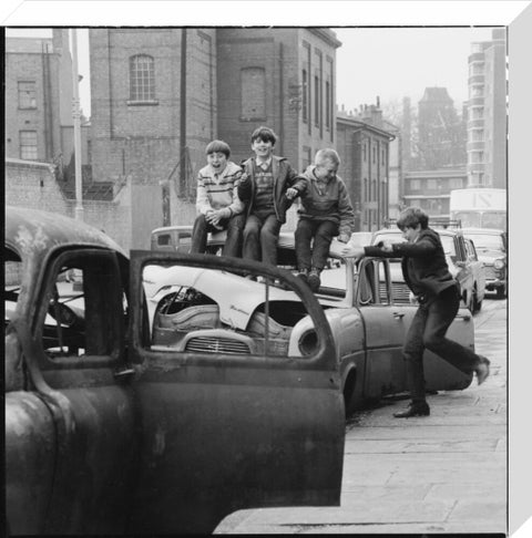 Four boys play on wrecked cars parked in the street 1967