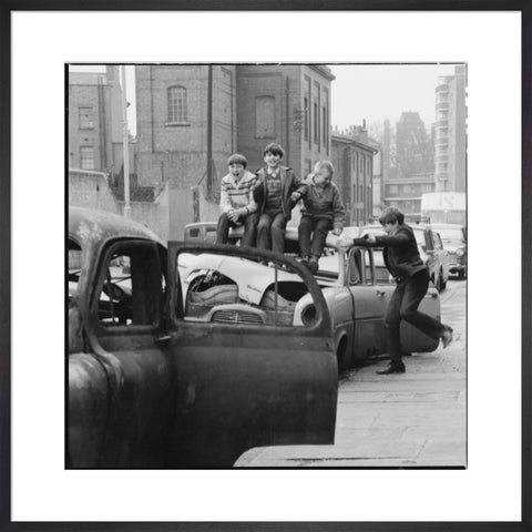 Four boys play on wrecked cars parked in the street 1967