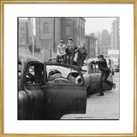 Four boys play on wrecked cars parked in the street 1967