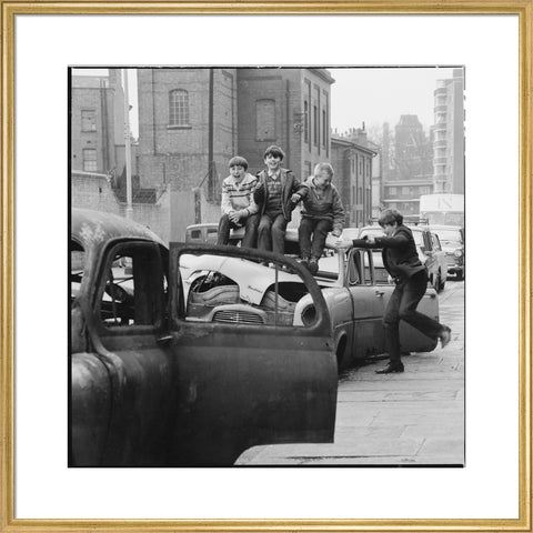 Four boys play on wrecked cars parked in the street 1967