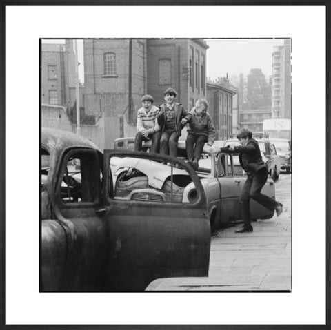 Four boys play on wrecked cars parked in the street 1967