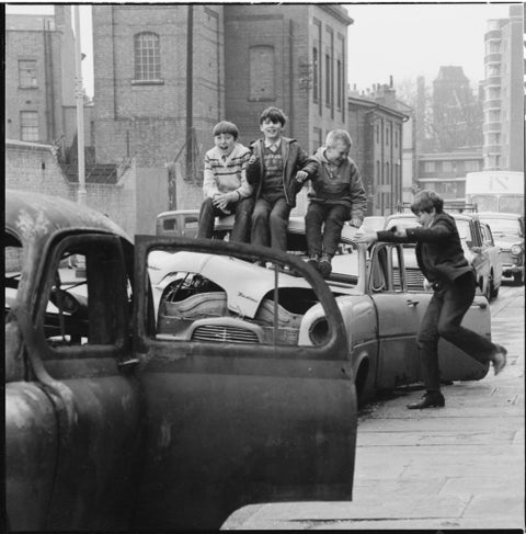 Four boys play on wrecked cars parked in the street 1967